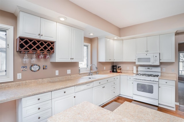 kitchen with white appliances, white cabinetry, light countertops, and a sink