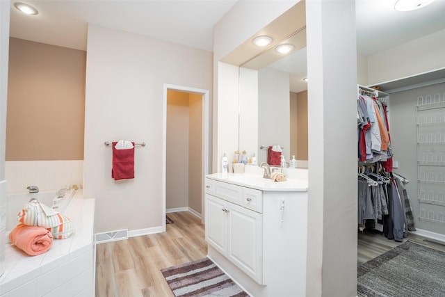 full bathroom with vanity, wood finished floors, visible vents, a walk in closet, and a garden tub