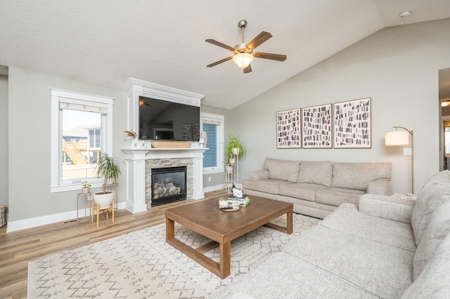 living area with baseboards, vaulted ceiling, a fireplace, wood finished floors, and a ceiling fan