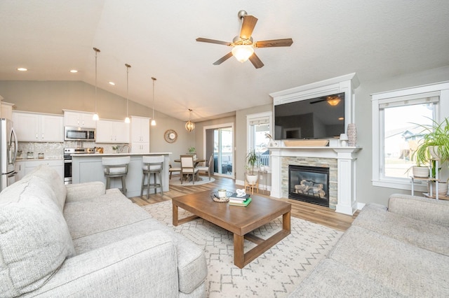 living area with lofted ceiling, light wood-style flooring, a ceiling fan, a fireplace, and baseboards