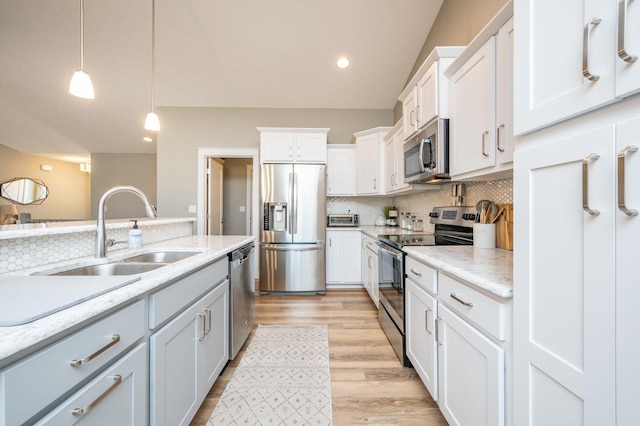 kitchen featuring a sink, decorative light fixtures, backsplash, light wood-style floors, and appliances with stainless steel finishes