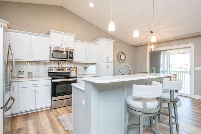 kitchen with a center island with sink, a kitchen breakfast bar, stainless steel appliances, white cabinets, and lofted ceiling