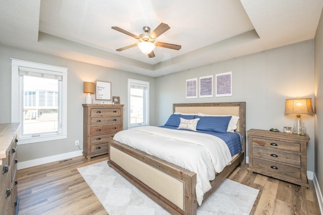 bedroom featuring a tray ceiling, light wood-style flooring, and baseboards