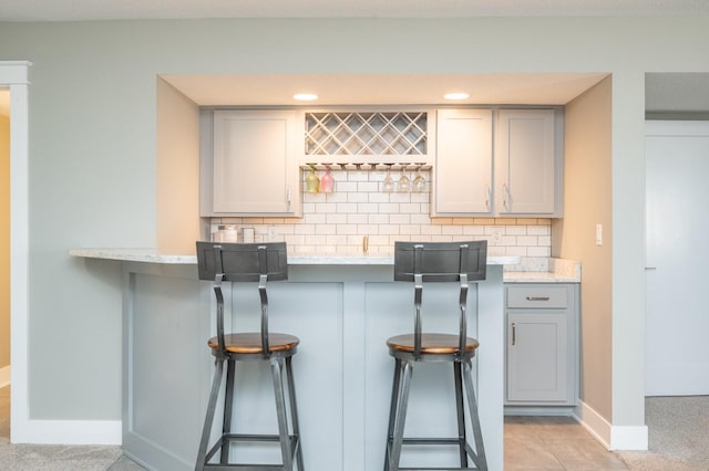 kitchen featuring a breakfast bar, gray cabinetry, decorative backsplash, baseboards, and light stone countertops