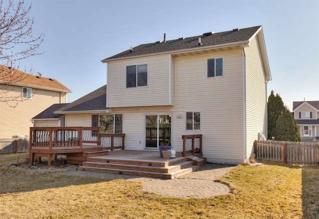 rear view of house with a yard, a shingled roof, a wooden deck, and fence