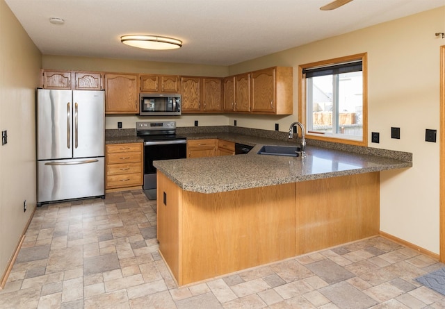 kitchen featuring baseboards, a peninsula, a sink, stainless steel appliances, and stone finish flooring