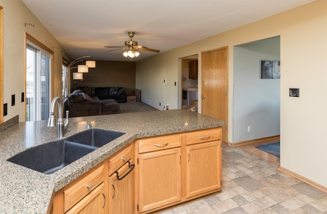 kitchen with baseboards, ceiling fan, open floor plan, stone tile floors, and a sink