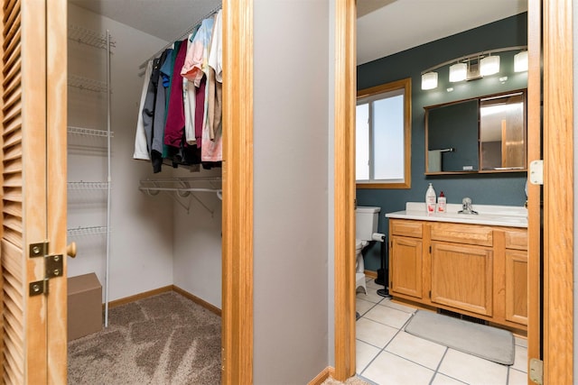 bathroom with tile patterned flooring, vanity, a walk in closet, and baseboards