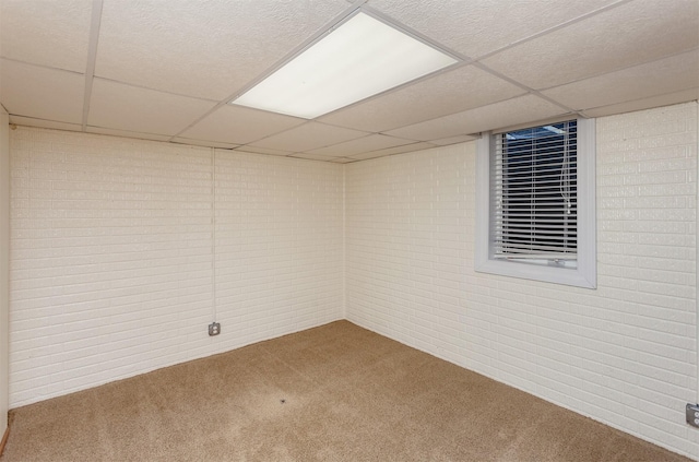 finished basement featuring a drop ceiling, carpet, and brick wall