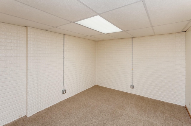 finished basement featuring brick wall, a drop ceiling, and carpet floors