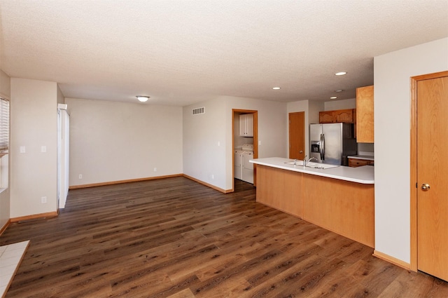 kitchen with washing machine and clothes dryer, stainless steel fridge with ice dispenser, a peninsula, dark wood-style floors, and a sink