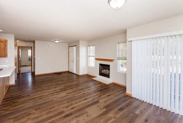 unfurnished living room with a textured ceiling, baseboards, dark wood-type flooring, and a tile fireplace