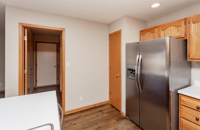 kitchen featuring light wood-type flooring, stainless steel refrigerator with ice dispenser, recessed lighting, light countertops, and baseboards