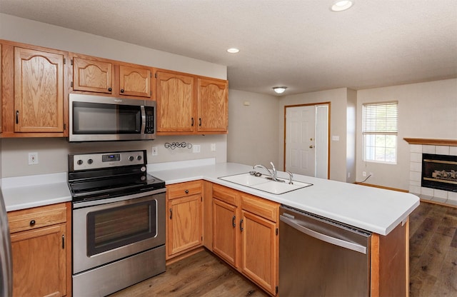 kitchen with a sink, stainless steel appliances, a peninsula, and dark wood-style floors