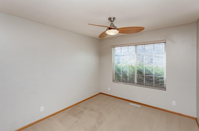 empty room featuring a textured ceiling, a ceiling fan, light colored carpet, and baseboards