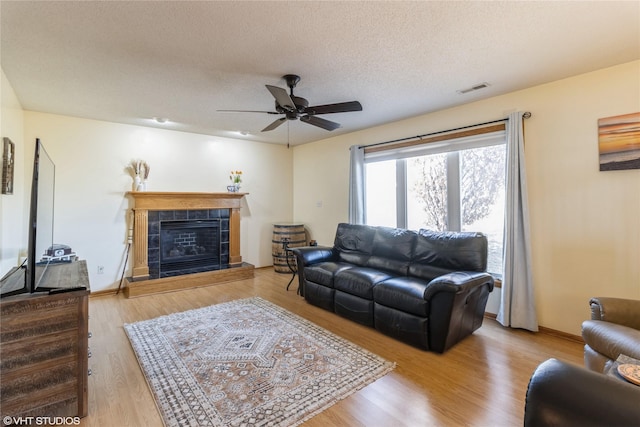 living area featuring visible vents, a textured ceiling, wood finished floors, ceiling fan, and a tile fireplace