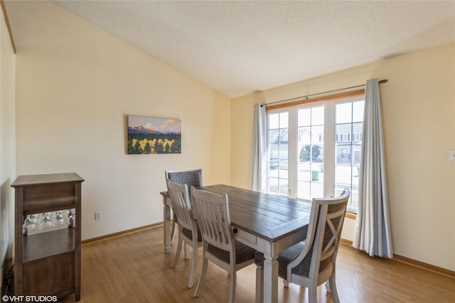 dining space featuring a textured ceiling, baseboards, lofted ceiling, and wood finished floors