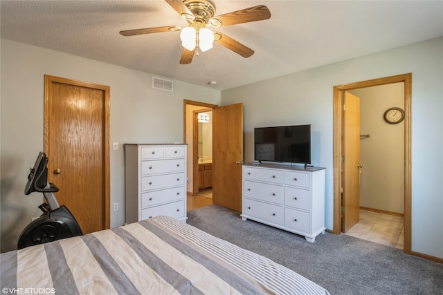 bedroom featuring visible vents, light carpet, ensuite bath, a textured ceiling, and a ceiling fan