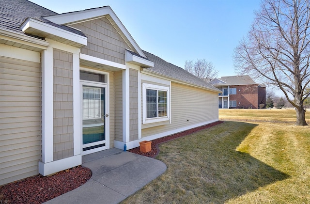 doorway to property featuring a lawn and a shingled roof