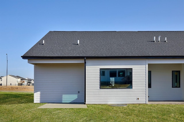 back of house with a lawn and roof with shingles