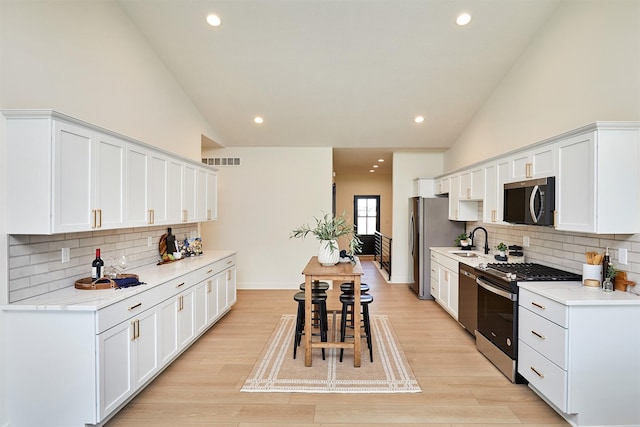 kitchen featuring visible vents, a sink, appliances with stainless steel finishes, white cabinetry, and light wood-type flooring