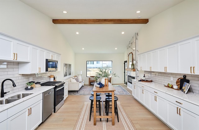 kitchen featuring a sink, stainless steel appliances, beamed ceiling, and white cabinets