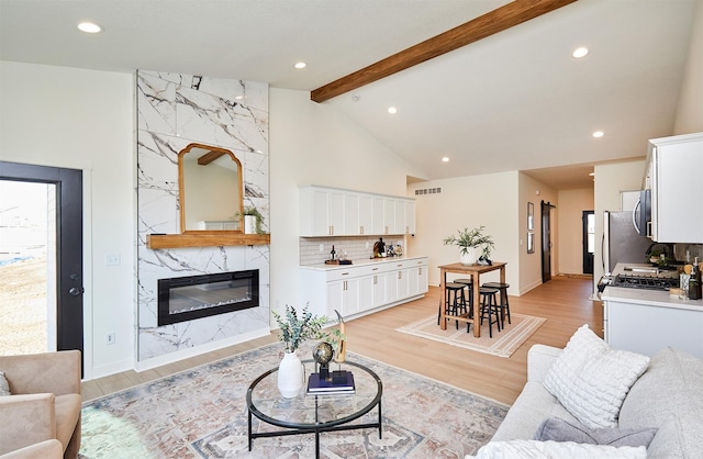 living room featuring visible vents, vaulted ceiling with beams, a premium fireplace, recessed lighting, and light wood-style flooring