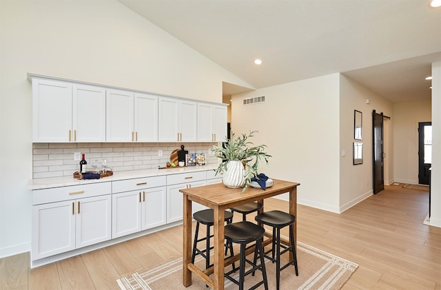 kitchen with visible vents, light countertops, vaulted ceiling, light wood-type flooring, and backsplash