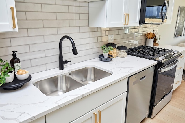 kitchen with light stone counters, decorative backsplash, stainless steel appliances, white cabinetry, and a sink