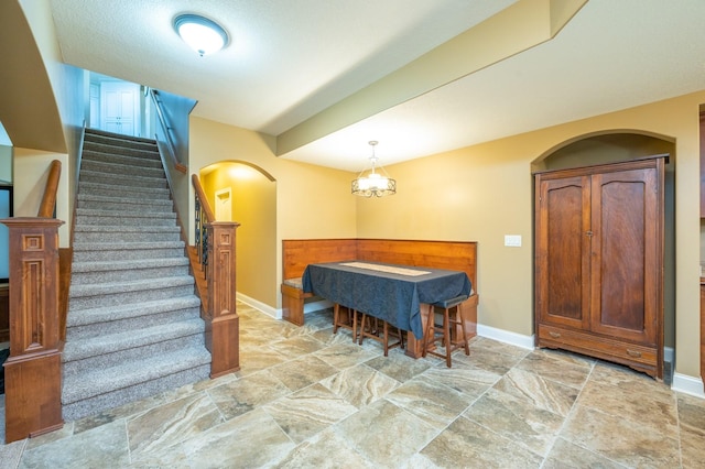 dining room with arched walkways, an inviting chandelier, stairs, and baseboards