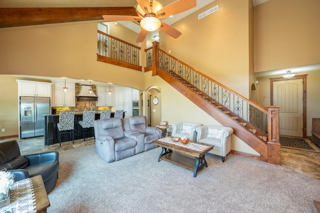 carpeted living area with visible vents, beam ceiling, a ceiling fan, stairway, and arched walkways