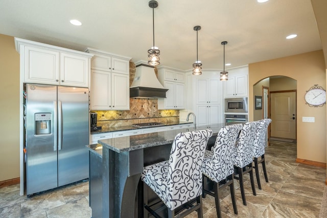 kitchen featuring premium range hood, arched walkways, stainless steel appliances, a kitchen breakfast bar, and backsplash