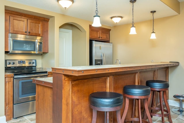 kitchen featuring brown cabinets, stone finish flooring, stainless steel appliances, and a breakfast bar area