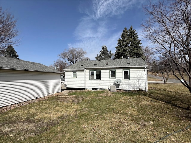 rear view of property with a yard, cooling unit, and a shingled roof