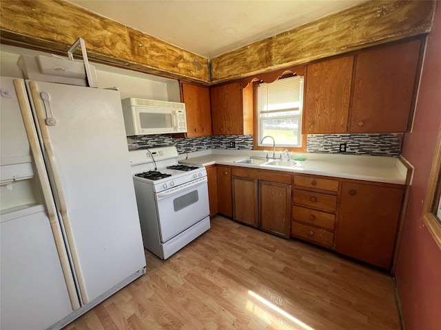 kitchen featuring white appliances, brown cabinetry, light wood-style flooring, a sink, and light countertops