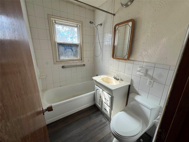 bathroom featuring toilet, wood finished floors, vanity, tile walls, and shower / bathtub combination