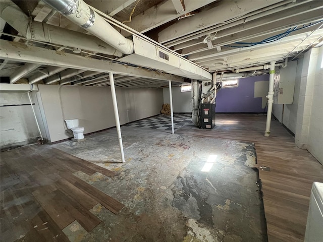 unfinished basement with visible vents, heating unit, and wood finished floors