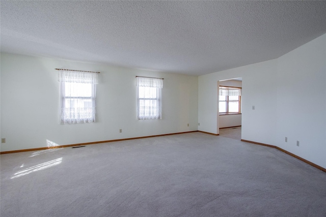 spare room featuring visible vents, baseboards, light colored carpet, and a textured ceiling