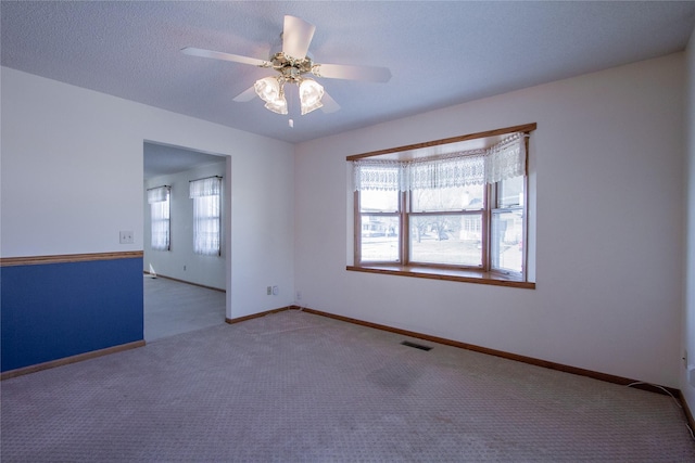 empty room with visible vents, baseboards, carpet floors, a textured ceiling, and a ceiling fan