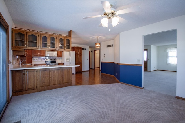 kitchen featuring brown cabinets, white appliances, a peninsula, dark colored carpet, and glass insert cabinets