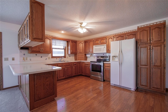 kitchen with white appliances, a ceiling fan, wood finished floors, a peninsula, and brown cabinets