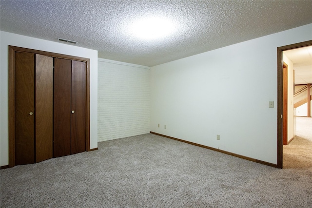 unfurnished bedroom with visible vents, a textured ceiling, a closet, brick wall, and carpet flooring