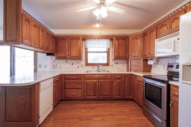 kitchen featuring white appliances, a peninsula, brown cabinets, and a sink