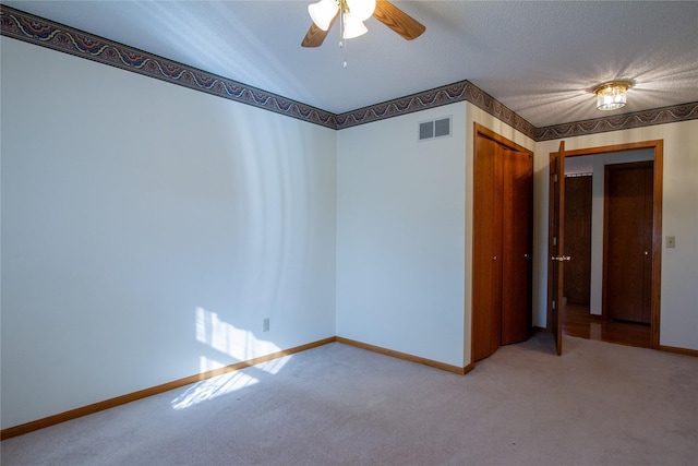 carpeted empty room with a textured ceiling, baseboards, visible vents, and ceiling fan