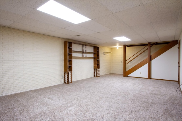 finished below grade area with a drop ceiling, carpet, and brick wall