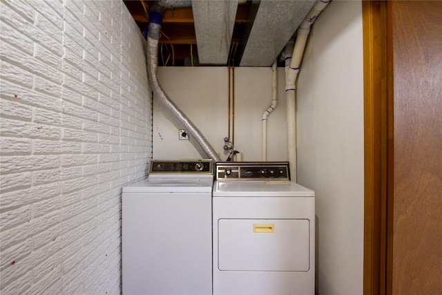 washroom with brick wall, laundry area, and washing machine and clothes dryer