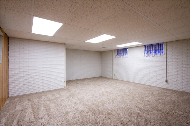 finished basement with a drop ceiling, brick wall, and carpet flooring