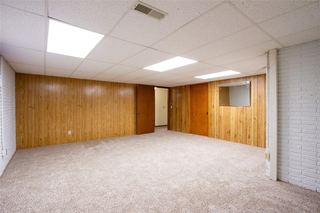 finished basement with a drop ceiling, visible vents, carpet floors, and wooden walls