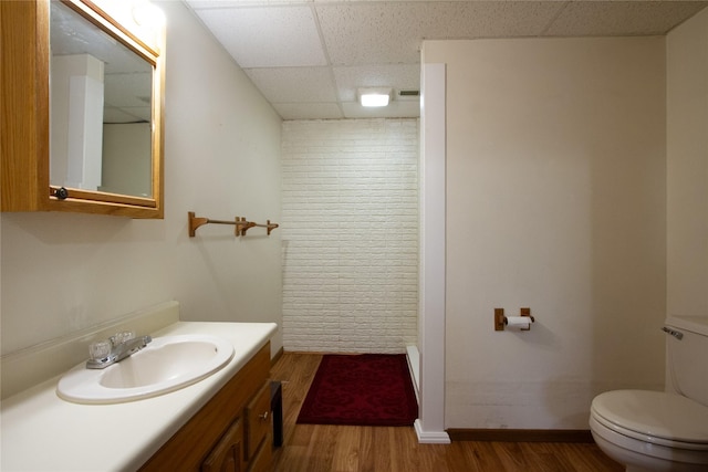 bathroom with baseboards, toilet, wood finished floors, vanity, and a paneled ceiling