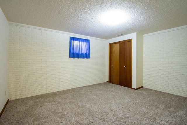 unfurnished bedroom with visible vents, a textured ceiling, a closet, brick wall, and carpet flooring